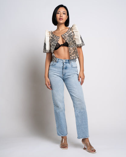 Woman wears ivory Leonora bolero with bralette and denim, exuding a cool, effortless vibe