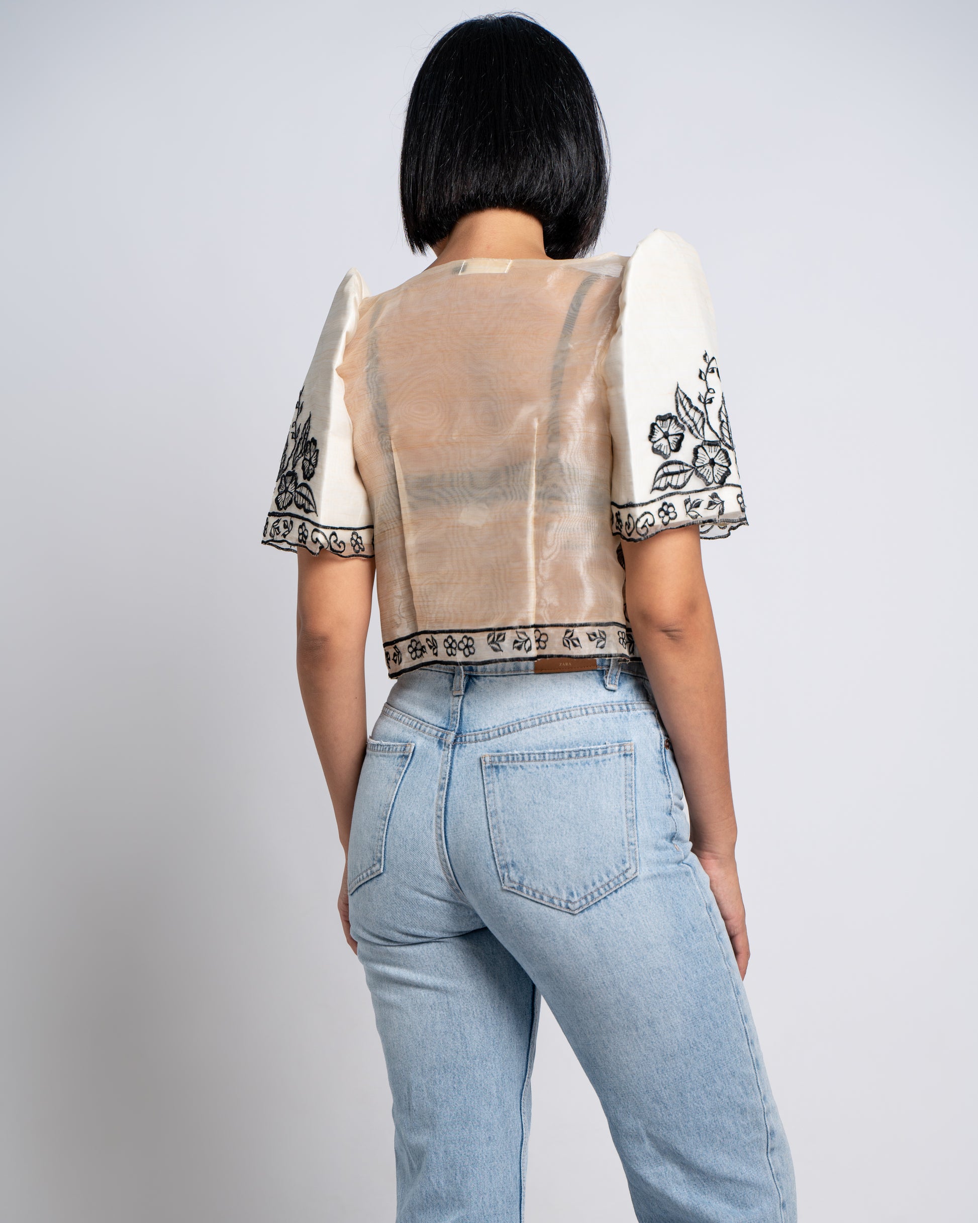 Woman wears ivory Leonora bolero with bralette and denim, exuding a cool, effortless vibe