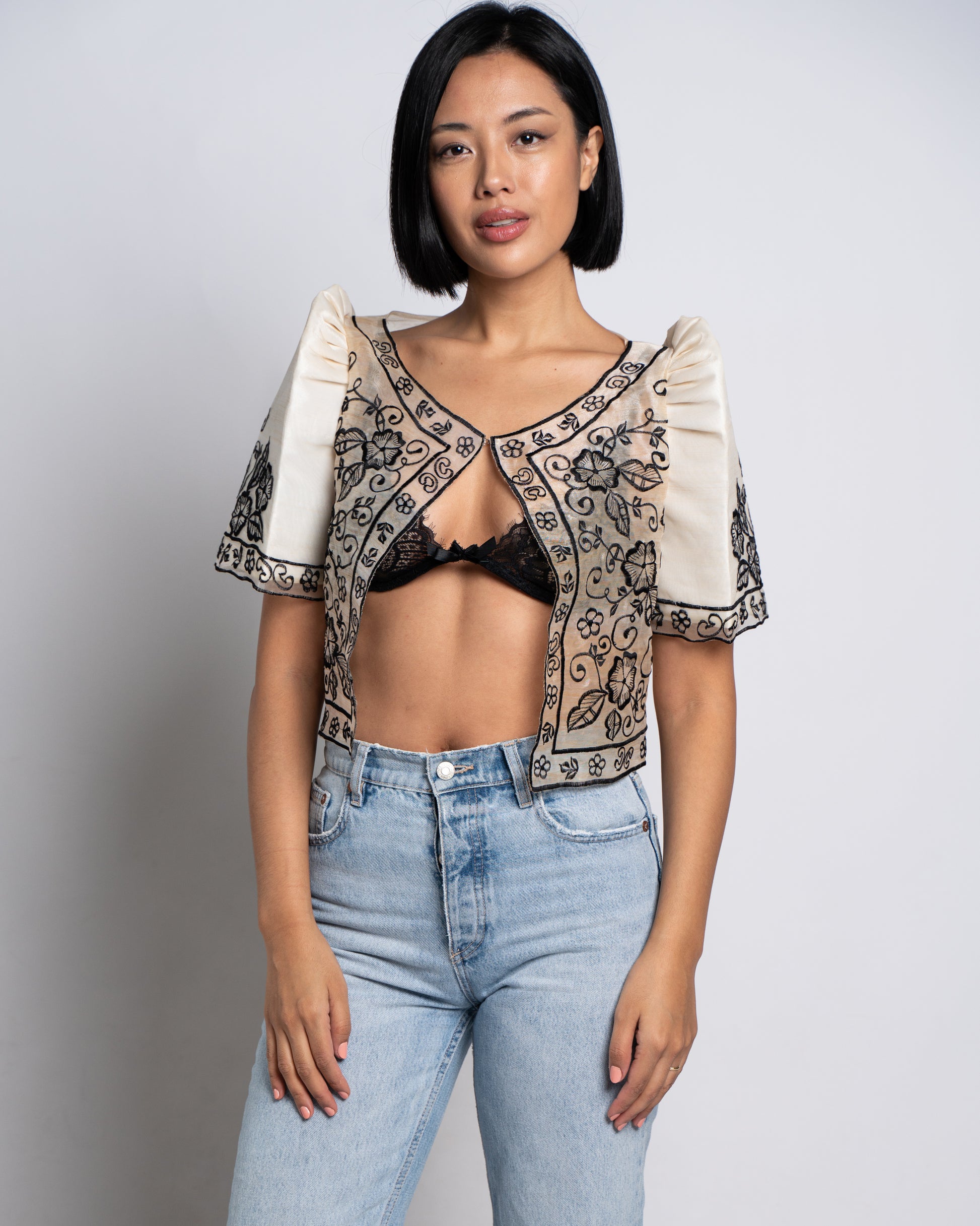 Woman wears ivory Leonora bolero with bralette and denim, exuding a cool, effortless vibe